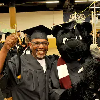 Student in cap and gown beside the Trailblazer Bear