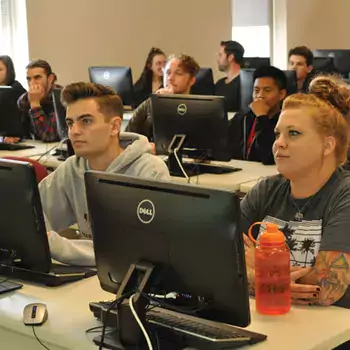 A bunch of students sitting at desks with computer monitors in a classroom.