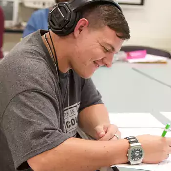 Student with headphones sitting at a desk writing