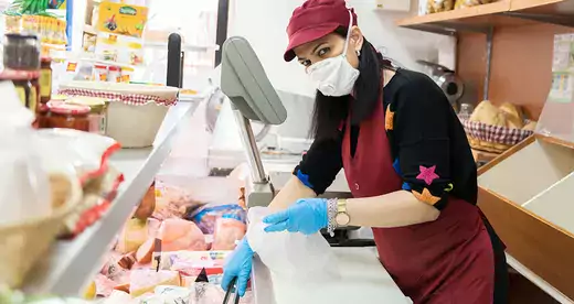 Woman behind food counter wearing gloves and mask