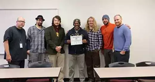 Heath Moody and his students in the Issues In Sustainability class against a wall with a certificate.