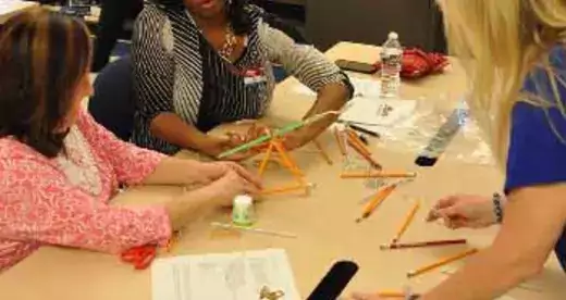 Three women at a table with materials for building a catapult.