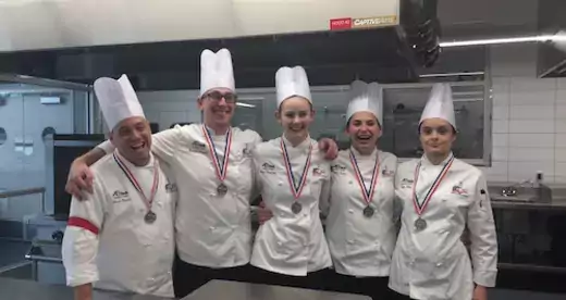 Five students in chef clothing in a kitchen