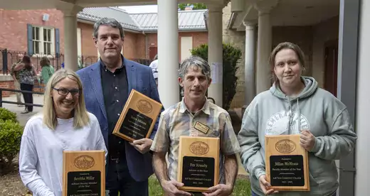 Four people holding plaques standing outside