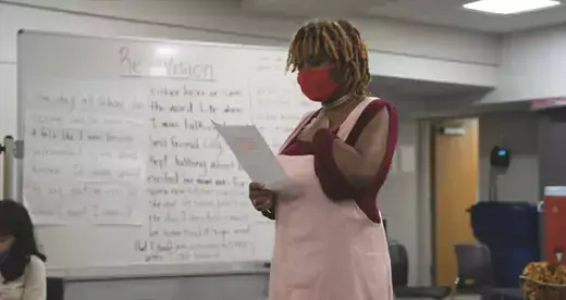 Young woman in mask standing reading a paper in a classroom