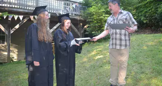 HIGH SCHOOL HANDOFF: Claire Bowling, left, and Amelia Darnell receive their high school diplomas in July 2019 from Chuck Bowling, who served as principal of their home school, Parkview Academy. Photo by Roger Darnell