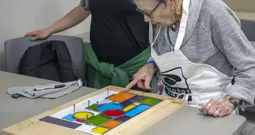 Older woman with stained glass project on table