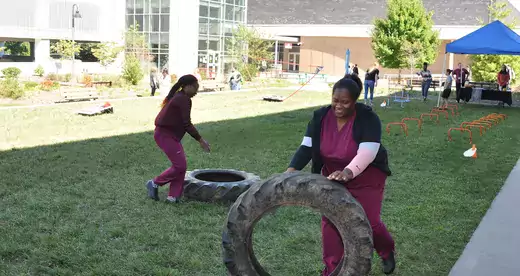 Two students in scrubs rolling tires on grass