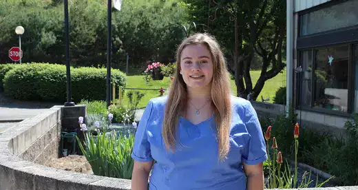 Young woman in scrubs standing in front of garden
