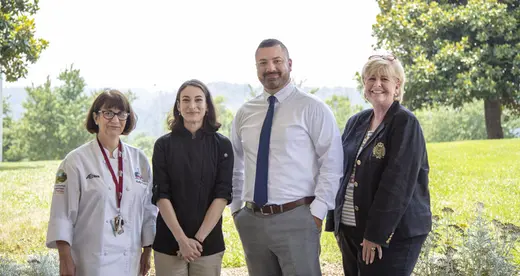Four people standing outside near trees