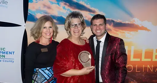 Two women and a man with an award