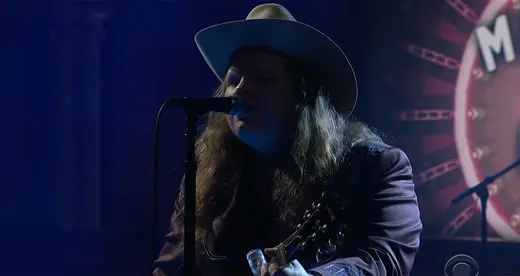 Man behind microphone holding a guitar