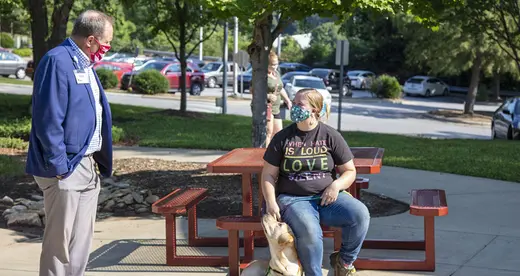 John Gossett standing in front of a student at a picnic table with dog sitting at student's feet. 