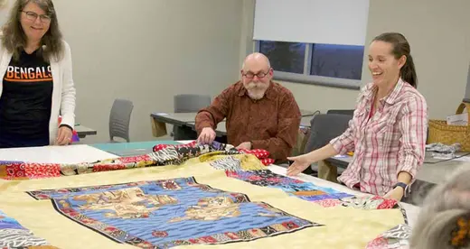 Three people at a table with a quilt