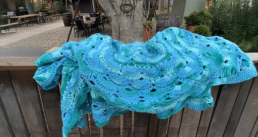 Crocheted green and blue blanket on a fence. 