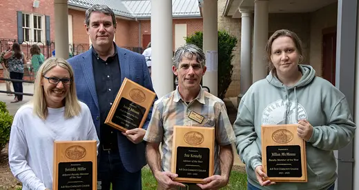 Four people holding plaques standing outside