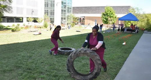Two students in scrubs rolling tires on grass