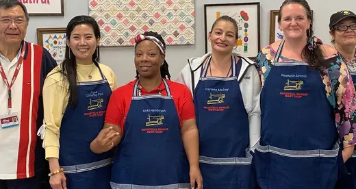 Six men and women in blue aprons standing