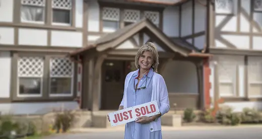 Anne Rasheed in front of a house holding a sold sign