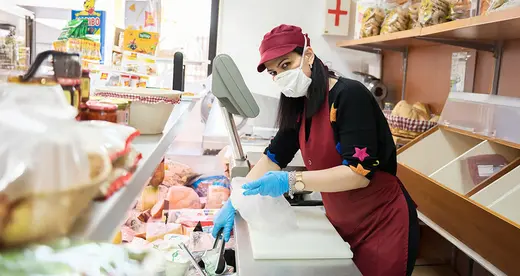 Woman behind food counter wearing gloves and mask