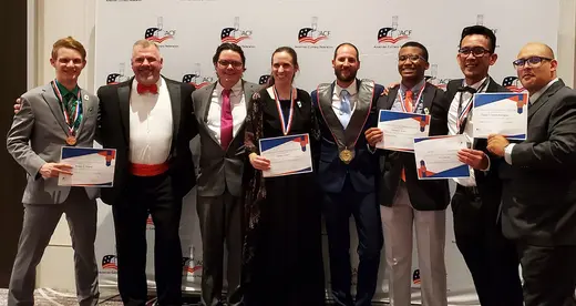 Eight people in formal wear standing in front of a wall with ACF logos