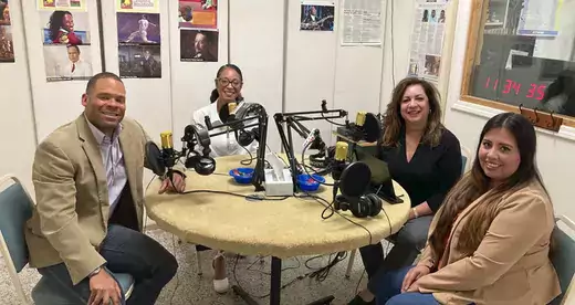 Four people sitting in front of a table with microphones