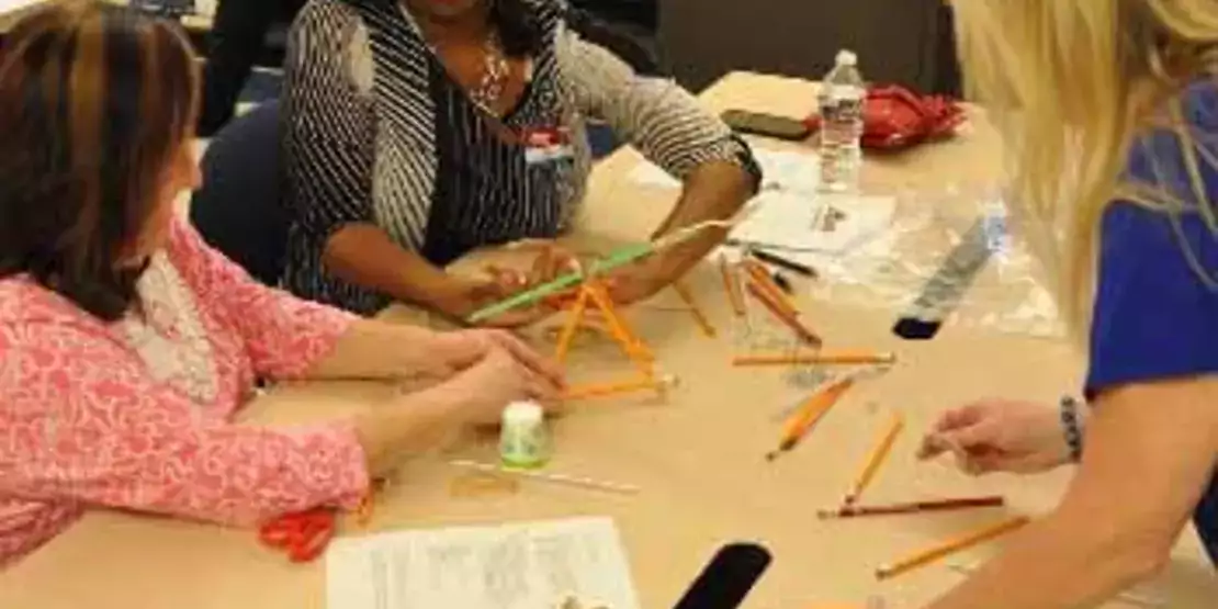 Three women at a table with materials for building a catapult.