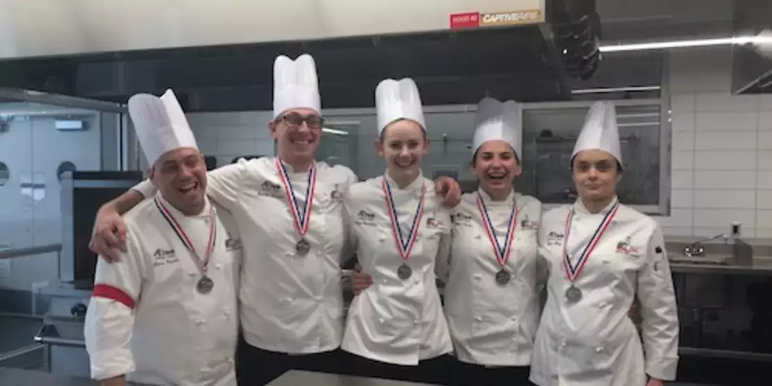 Five students in chef clothing in a kitchen