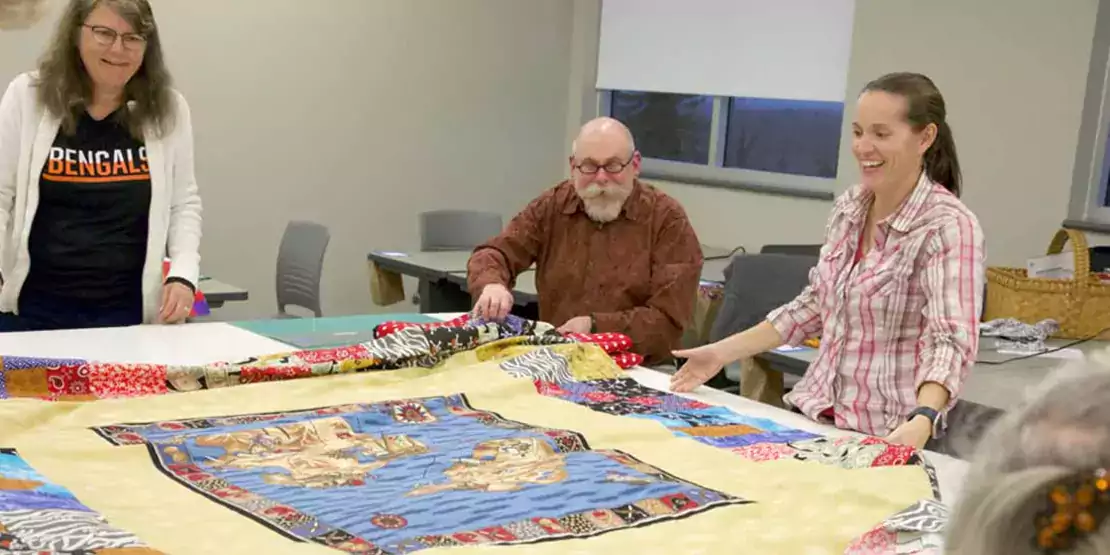 Three people at a table with a quilt