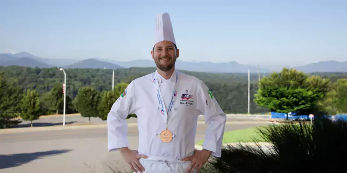 A chef wearing his uniform with a medal around his neck. 