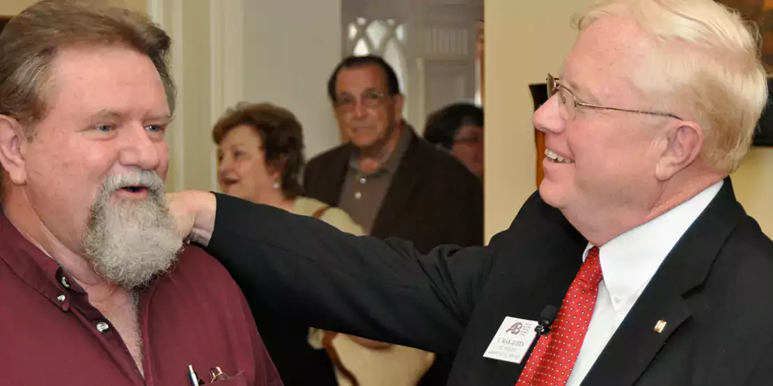 Two men speaking to each other. One has his hand on the other's shoulder