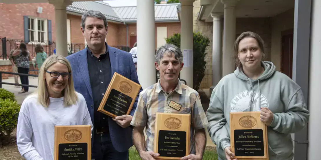 Four people holding plaques standing outside
