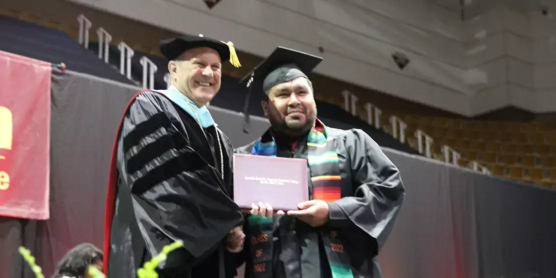 Dr. Gossett handing a diploma to male student at commencement