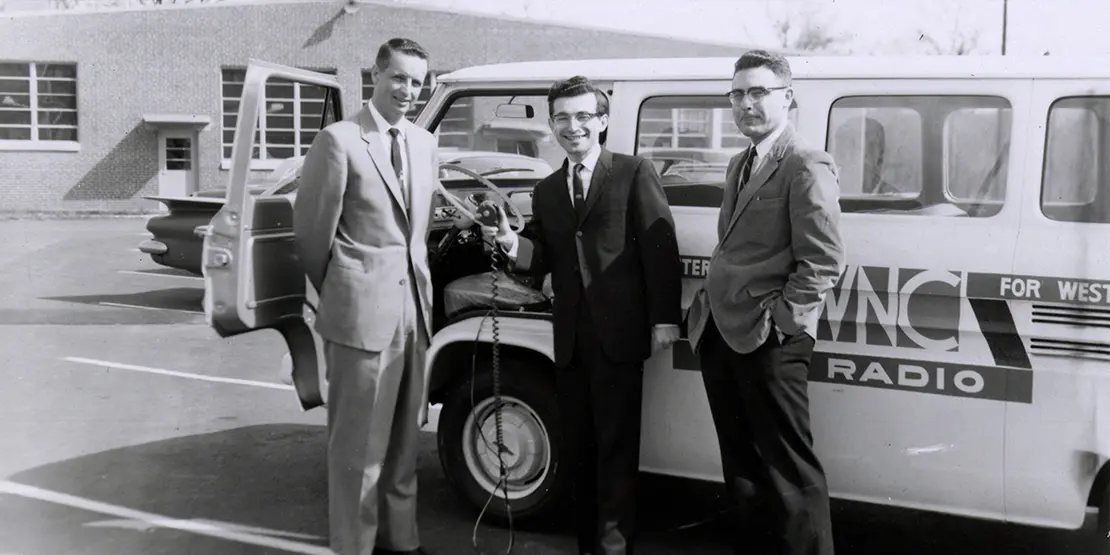 Three men in front of a radio broadcasting van