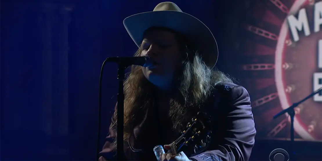 Man behind microphone holding a guitar