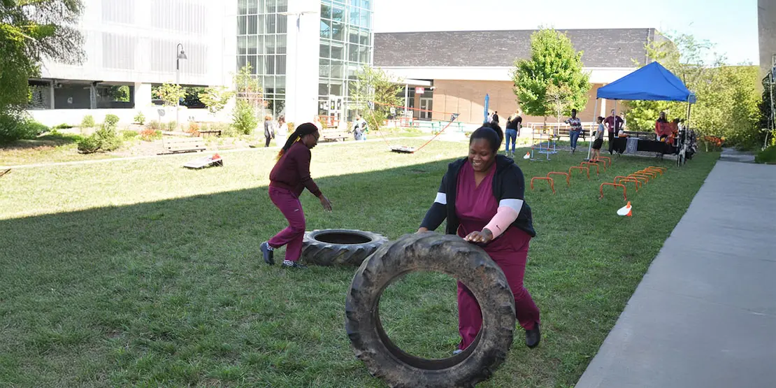 Two students in scrubs rolling tires on grass