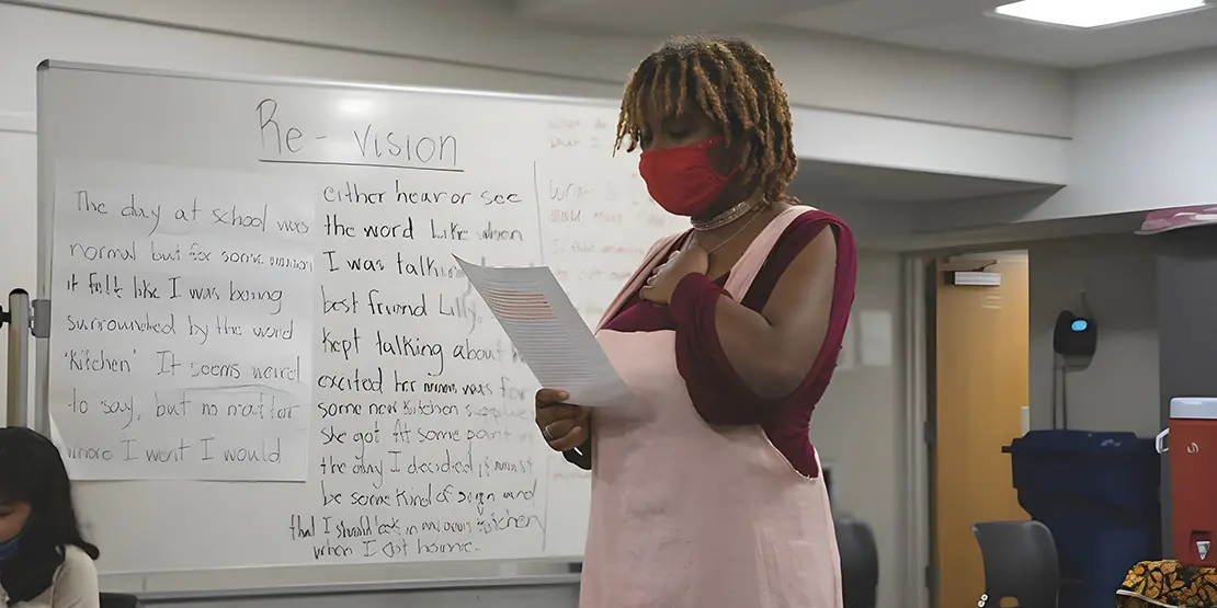 Young woman in mask standing reading a paper in a classroom