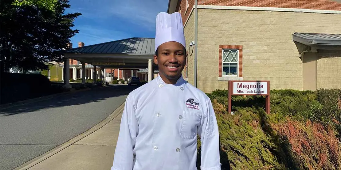 Young man in chef's uniform standing outside a building