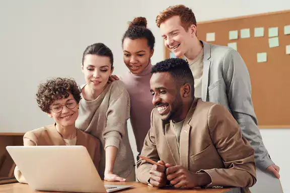 A group of smiling people looking at a laptop
