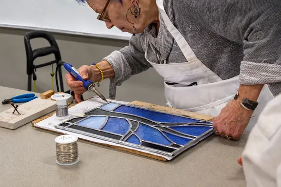 A craftsperson soldering a blue stained-glass panel