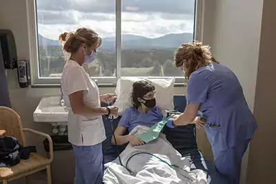 Two women standing by an occupied hospital bed