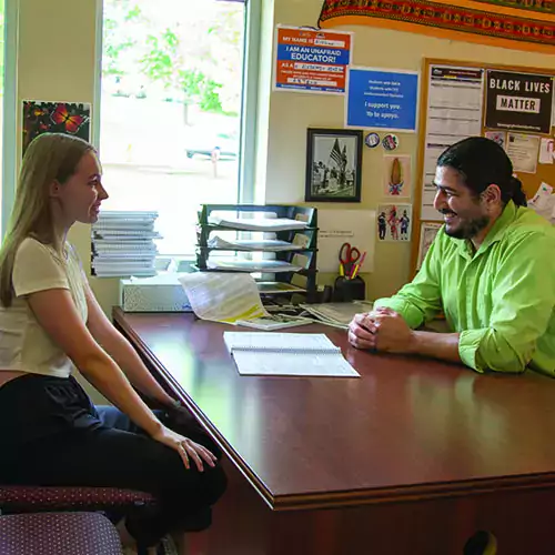 Teacher sitting at a desk advising a student.