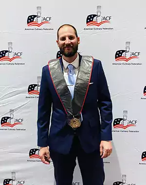 Man standing in front of wall wearing a medallion