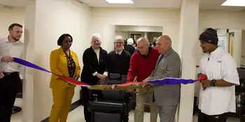 Seven people in front of a barber chair cutting a ribbon