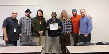Heath Moody and his students in the Issues In Sustainability class against a wall with a certificate.