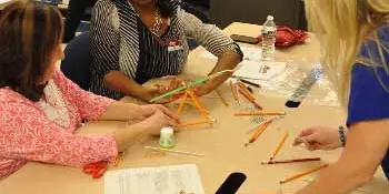 Three women at a table with materials for building a catapult.