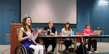 Madeline Delp in a wheelchair in front of three women at a table. 