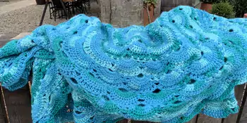 Crocheted green and blue blanket on a fence. 