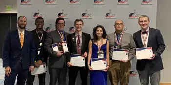 Seven well dressed chefs standing in front of a wall holding certficates