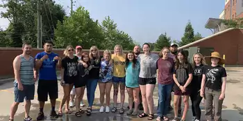 A group of wet students standing on a concrete surface. 